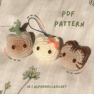 May include: Three crocheted cat keychains with different colored fur. The cats are brown, white, and brown and orange. The keychains are attached to a black string. The text "PDF PATTERN" is written in green letters on a white background. The text "IG | ASPHODELCROCHET" is written in black letters on a white background.