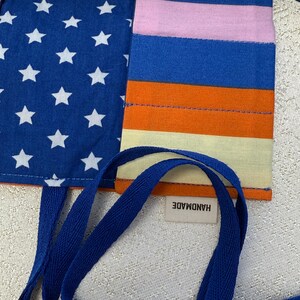 May include: A blue and white star patterned fabric pouch with a multi-colored striped fabric panel. The pouch has a blue fabric strap and a white tag that says "HANDMADE".