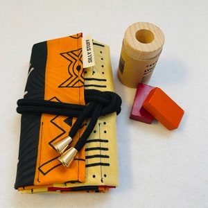 May include: A black and yellow fabric pouch with a black cord and gold toggles. The pouch is folded and has a label that says "Silly Stuff". There are two red and orange rectangular blocks next to the pouch.