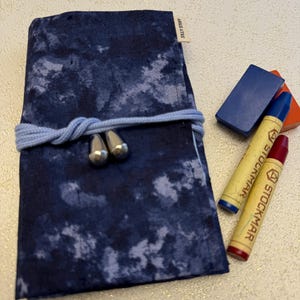 May include: A blue fabric pouch with a tie closure and silver accents. The pouch is filled with crayons and a blue eraser. The pouch has the text "SELLA STORE" printed on the side.