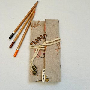 Op de afbeelding: Een beige linnen potlood etui met een bruin en oranje bloemenpatroon en een bruin gezichtsontwerp. Het etui heeft een witte trekkoord sluiting en een bruin lederen label met de tekst "Silly Stuff".