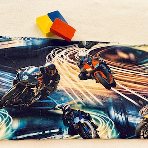 May include: A black and blue fabric with a repeating pattern of motorcycles racing on a track with streaks of light. The fabric has a dark background with bright yellow and orange streaks of light.