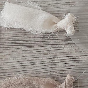 May include: A vertical arrangement of five circular clear acrylic tags, each tied with a strip of frayed-edge fabric in varying shades of white, cream, beige, light tan, and burnt orange, secured with a simple knot through a small hole.