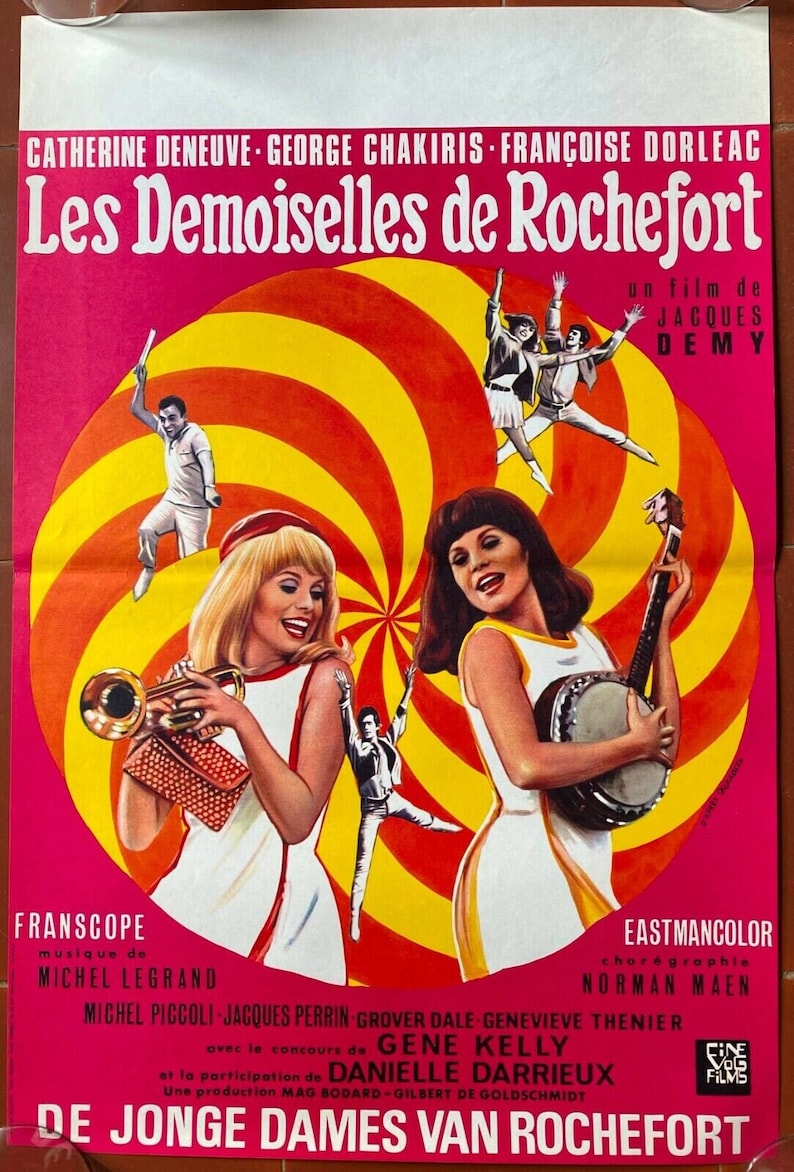 May include: A vintage movie poster for "Les Demoiselles de Rochefort" in pink, yellow, and white. The poster features two women, one with a trumpet and the other with a banjo, against a spiral background. The film title and credits are displayed.