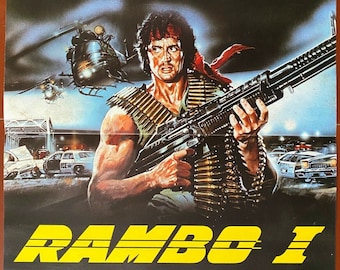 May include: A movie poster for the action film "Rambo: First Blood" starring Sylvester Stallone. The poster features a close-up of Stallone holding a machine gun, with a helicopter and police cars in the background. The text on the poster reads "Sylvester Stallone" and "Rambo I (Rambo "First Blood")".
