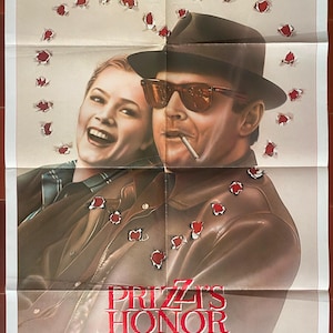 Puede incluir: Cartel de la película "El honor de los Prizzi" con Jack Nicholson y Kathleen Turner. El cartel tiene un fondo beige con gráficos de agujeros de bala. Los actores están en el centro, con el título en rojo debajo.