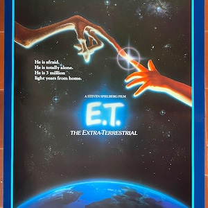 Könnte beinhalten: Ein Filmplakat für den Film "E.T. der Außerirdische" mit einer Nahaufnahme einer außerirdischen Hand, die sich einer menschlichen Hand entgegenstreckt. Das Plakat hat einen dunkelblauen Hintergrund mit Sternen und einem Planeten im Hintergrund. Der Text auf dem Plakat lautet "Die Geschichte, die die Welt berührte." und "Ein Film von Steven Spielberg E.T. der Außerirdische."