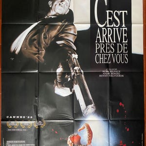 May include: A movie poster for the French film "C'est Arrive Pres De Chez Vous" (It Happened Near You). The poster features a man holding a gun, with a bloody mouth in the background. The text on the poster reads "C'est Arrive Pres De Chez Vous" and "Un Film De Remy Belvaux, Andre Bonzel, Benoit Poelvoorde".