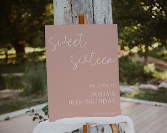 May include: A pink welcome sign with white text that reads "Sweet Sixteen, Welcome to Emilia's 16th Birthday, April 24th, 202X". The sign is on a wooden easel.