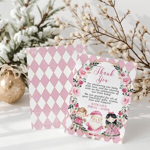 Puede incluir: Tarjeta de agradecimiento de baby shower rosa y blanca con un patrón de diamantes. La parte delantera presenta una corona floral con texto e ilustraciones de una niña, Papá Noel y otra niña. El texto dice "Gracias".