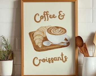 May include: A framed print featuring a watercolor illustration of coffee and croissants. The image shows a white coffee cup with latte art, a croissant, and a spoon on a wooden tray. The words "Coffee & Croissants" are written in brown script.
