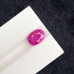 May include: A vibrant pink oval-shaped gemstone, likely a ruby, displayed on a white background.