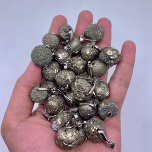 Könnte beinhalten: Eine Sammlung von 20 Pyrit-Edelstein-Anhängern mit silberfarbenen Metallösen. Die Anhänger sind rund und haben eine raue, strukturierte Oberfläche.