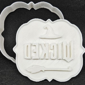 Puede incluir: Cortador de galletas de plástico blanco en forma de letrero con la palabra "Wicked" y un sombrero de bruja en la parte superior.