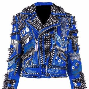 Puede incluir: Una chaqueta de cuero azul con tachuelas plateadas y cierre de cremallera. La chaqueta tiene un cinturón con tachuelas plateadas y una variedad de parches con texto y gráficos.