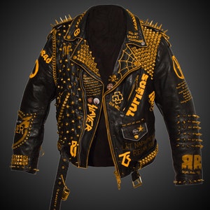 Peut inclure: Veste en cuir noir avec des clous et des pointes dorés. La veste comporte divers patchs et inscriptions en jaune, notamment "TUTISAS", "ICH WILL", "THE ART OF WAR" et "LAT NAPALMEN REGNA NE".