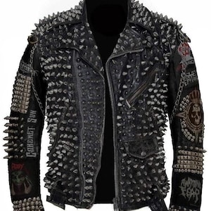 Può includere: Giacca di pelle nera con borchie e toppe in metallo argentato. La giacca ha una chiusura a zip e un colletto. Le toppe includono un teschio, una corona e le parole "God's Sun" e "Chaos Fear".