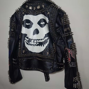 Pode incluir: Jaqueta de couro preta com tachas prateadas e um gr&aacute;fico de caveira Misfits nas costas. A jaqueta tem patches nas mangas.