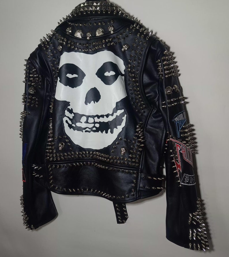 Pode incluir: Jaqueta de couro preta com tachas prateadas e um gr&aacute;fico de caveira Misfits nas costas. A jaqueta tem patches nas mangas.