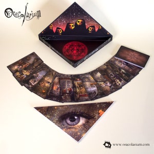 May include: A tarot card deck with a black, triangular box featuring skull illustrations and a red geometric symbol. The cards are fanned out, displaying detailed fantasy art. A triangular card with an eye design is also present.