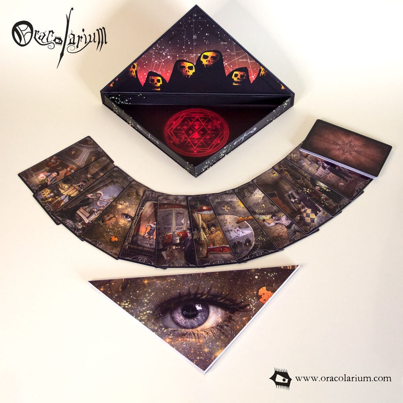 May include: A tarot card deck with a black, triangular box featuring skull illustrations and a red geometric symbol. The cards are fanned out, displaying detailed fantasy art. A triangular card with an eye design is also present.