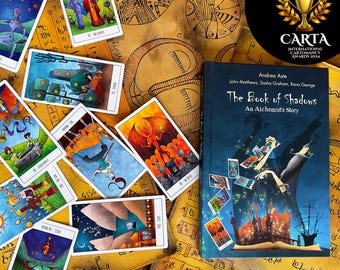 May include: A tarot deck with colorful illustrations on each card, laid out on a table with a book titled "The Book of Shadows: An Alchemist's Story" by Andrea Aste, John Matthews, Sasha Graham, and Rana George. The book is blue with gold lettering and a colorful illustration of a hand holding tarot cards.