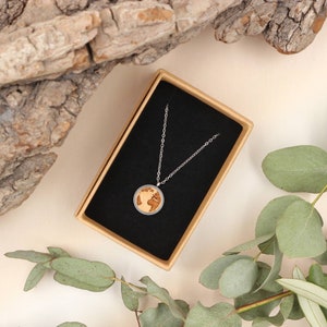 May include: A silver chain necklace with a round pendant featuring a wood-grain globe design. The necklace is displayed in a black velvet box with a brown exterior.