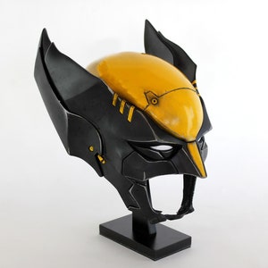 Puede incluir: Un casco negro y amarillo con un diseño detallado. El casco está en un soporte negro.