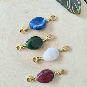 Può includere: Quattro ciondoli in pietra colorati con chiusure color oro. I ciondoli sono nelle tonalità di blu, verde, bianco e bordeaux. I ciondoli sono di forma ovale e hanno un aspetto marmorizzato. Le chiusure sono attaccate a ciascuna estremità della pietra.