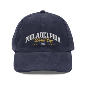 May include: Navy blue corduroy baseball cap with the text "PHILADELPHIA World Cup 2026" embroidered in white and gold. The cap has a curved brim and a top button.