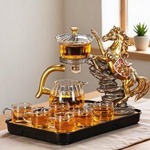 Puede incluir: Un juego de té con una tetera de cristal transparente y seis tazas pequeñas de cristal sobre una bandeja negra. Una escultura de caballo de color dorado se alza sobre una base rocosa, sosteniendo un infusor de cristal sobre la tetera.