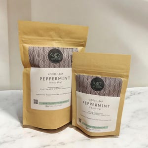 May include: Two brown paper pouches of loose leaf peppermint tea. The larger pouch is labeled "1.8 oz / 51 gr" and the smaller pouch is labeled "0.6 oz / 17 gr". Each pouch has a white label with the text "PEPPERMINT" and "TEAS OF CEYLON".