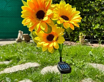 Könnte beinhalten: Ein solarbetriebener Gartenpfahl mit drei künstlichen gelben Sonnenblumen. Der Pfahl hat ein schwarzes Solarpanel und eine silberne Metallstange.
