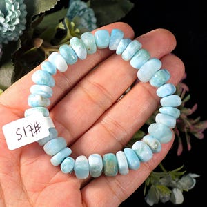 Puede incluir: Una pulsera el&aacute;stica compuesta por cuentas pulidas, irregulares y redondeadas de piedra Larimar azul claro y blanco. Las cuentas var&iacute;an en tama&ntilde;o y forma, mostrando vetas y degradados naturales. Se adjunta una peque&ntilde;a etiqueta blanca rectangular con el texto S17#.