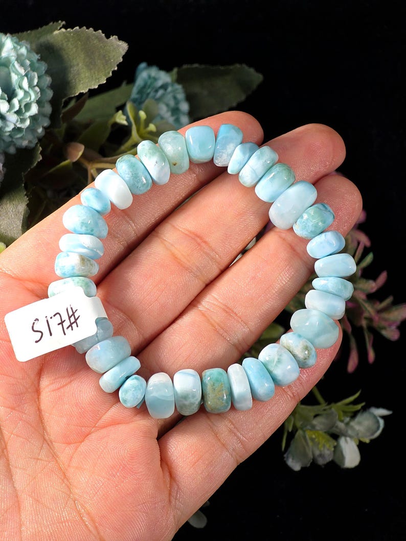 Puede incluir: Una pulsera el&aacute;stica compuesta por cuentas pulidas, irregulares y redondeadas de piedra Larimar azul claro y blanco. Las cuentas var&iacute;an en tama&ntilde;o y forma, mostrando vetas y degradados naturales. Se adjunta una peque&ntilde;a etiqueta blanca rectangular con el texto S17#.