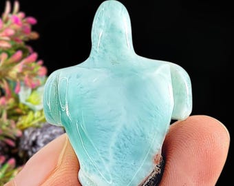 Könnte beinhalten: Eine geschnitzte, hellblaue Schildkrötenfigur aus Edelstein. Die Schildkröte ist hellblau mit weißen Marmorierungen. Die Figur wird in einer Hand vor einem schwarzen Hintergrund gehalten. Der Schildkrötenpanzer hat ein strukturiertes Aussehen.