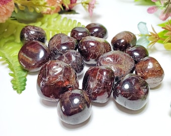 May include: A collection of tumbled red garnet stones. The stones are smooth and polished, with a deep red color. Garnet is a popular gemstone for jewelry and healing.
