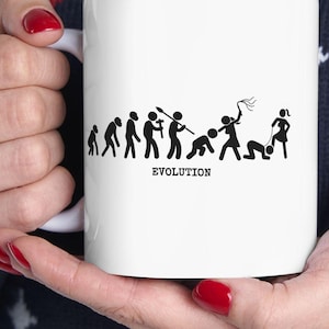 May include: White ceramic mug featuring a black and white graphic depicting the evolution of humans, with the word "EVOLUTION" below the figures. The mug is held by a person wearing a blue sweater with a reindeer pattern.