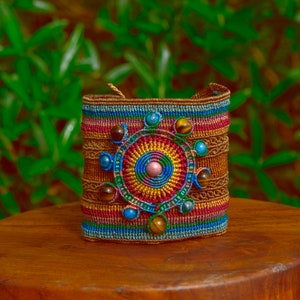 May include: A colorful woven bracelet with a circular design featuring tiger's eye and other gemstones. The bracelet is brown, red, blue, green, and yellow.