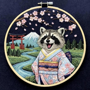 May include: Embroidered artwork featuring a raccoon wearing a kimono, set against a Japanese landscape with Mount Fuji, a red torii gate, and a flowing river. Cherry blossoms and green trees complete the scene, framed in a wooden hoop.
