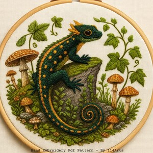Könnte beinhalten: Handgesticktes Kunstwerk in einem Holzrahmen, das eine grüne und gelbe Eidechse auf einem moosigen Felsen zeigt, umgeben von Pilzen und Blättern. Der Text "Hand Embroidery PDF Pattern - By 114Arts" ist unten zu sehen.