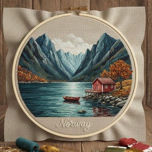 Può includere: Ricamo su telaio raffigurante un paesaggio norvegese. Il disegno include una capanna rossa, una barca e montagne riflesse nell'acqua. La parola "Norway" è ricamata sotto. Il telaio è posto su un tessuto neutro.