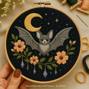 May include: Hand-stitched embroidery in a wooden hoop features a gray bat with outstretched wings, a yellow crescent moon, and orange flowers on a dark blue background. The text "Hand Embroidery Pdf Pattern - By 114Arts" is at the bottom.
