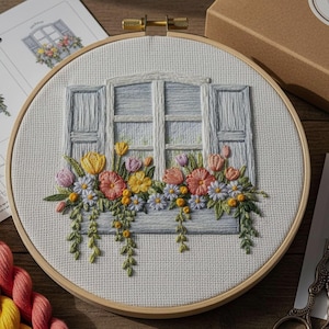 Pode incluir: Cena de janela floral bordada em um círculo de madeira. O design apresenta uma janela azul clara com persianas abertas e uma floreira transbordando de flores coloridas. O bordado inclui flores amarelas, rosas e laranjas com folhagem verde.