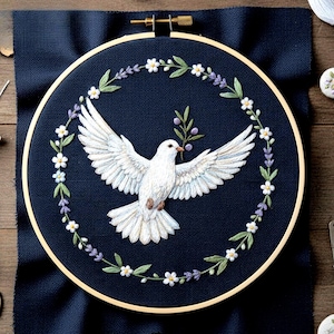 May include: Embroidered artwork featuring a white dove with outstretched wings, holding an olive branch. The dove is centered on a dark blue fabric, surrounded by a floral wreath in a wooden embroidery hoop. The embroidery includes white, green, and purple details.