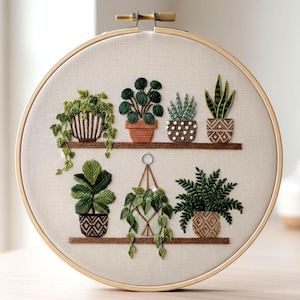 Könnte beinhalten: Gesticktes Stickrahmen-Kunstwerk mit einer Sammlung von Topfpflanzen auf Regalen. Die Pflanzen sind in verschiedenen Grüntönen gehalten, mit braunen Töpfen und Regalen. Die Stickerei ist vor einem neutralen Stoffhintergrund angebracht und von einem Holzreifen umrahmt.