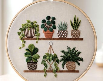 May include: Embroidered hoop art showing a selection of potted plants on shelves. The plants are in shades of green, with brown pots and shelves. The embroidery is set against a neutral fabric background, framed by a wooden hoop.