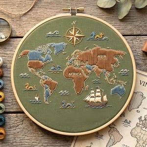 May include: Embroidered world map in a wooden hoop. The map features continents in brown and blue thread on a green background. A compass rose and a sailing ship are also embroidered. The hoop is approximately 10 inches in diameter.