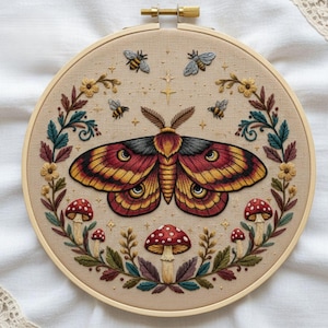 Può includere: Ricamo circolare in un cerchio di legno. Raffigura una grande falena con ali rosse e gialle, circondata da api, funghi ed elementi floreali. Lo sfondo è in tessuto beige, creando un design a tema natura.