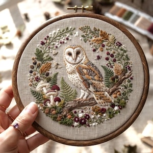 May include: A circular wooden embroidery hoop containing a linen fabric panel with a detailed needlework design of a barn owl perched on a branch. The owl is surrounded by a wreath of embroidered ferns, mushrooms, berries, and small flowers.